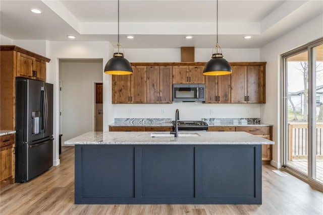 kitchen with light stone counters, an island with sink, hanging light fixtures, and appliances with stainless steel finishes