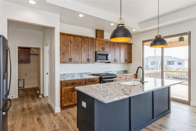 kitchen featuring a kitchen island with sink, sink, hanging light fixtures, appliances with stainless steel finishes, and light stone counters