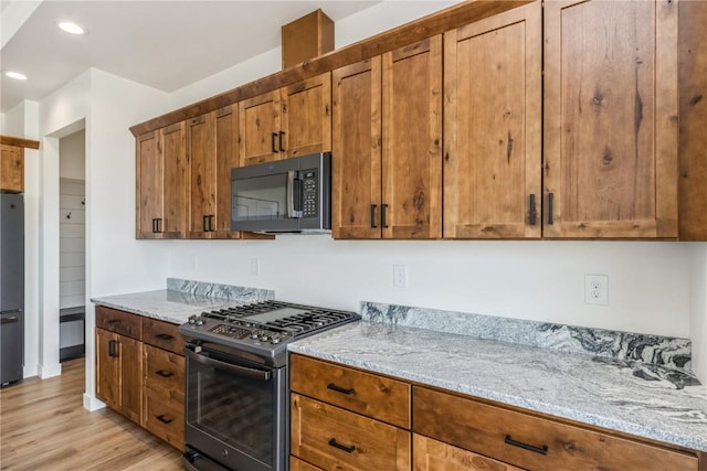 kitchen with light stone countertops, light wood-type flooring, and black appliances