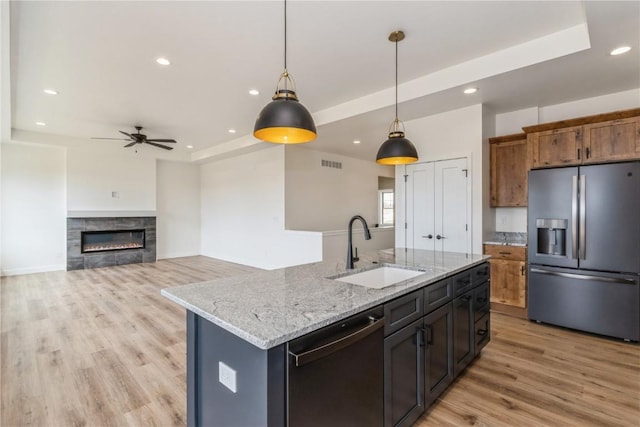 kitchen with a raised ceiling, sink, stainless steel appliances, and an island with sink