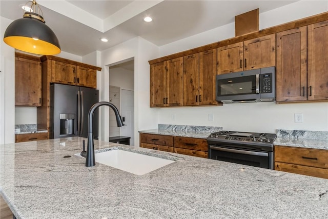 kitchen with light stone counters, sink, pendant lighting, and appliances with stainless steel finishes