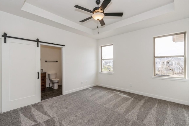 unfurnished bedroom with carpet flooring, ceiling fan, a barn door, connected bathroom, and a tray ceiling