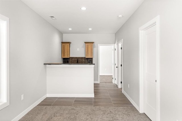 kitchen featuring kitchen peninsula, light brown cabinets, backsplash, and dark carpet