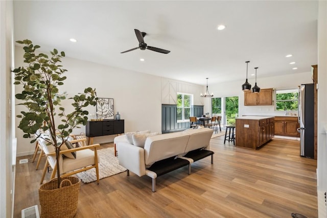 living room with ceiling fan with notable chandelier, light hardwood / wood-style floors, and sink