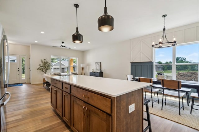 kitchen featuring stainless steel fridge, light wood-type flooring, ceiling fan with notable chandelier, decorative light fixtures, and a center island