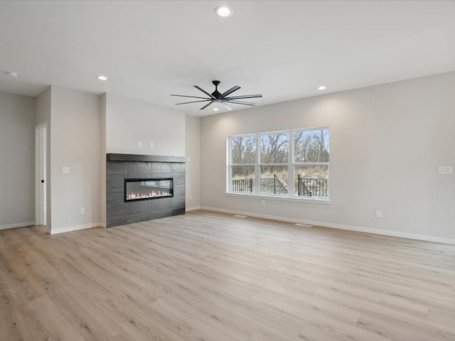 unfurnished living room featuring ceiling fan, a tile fireplace, and light hardwood / wood-style flooring