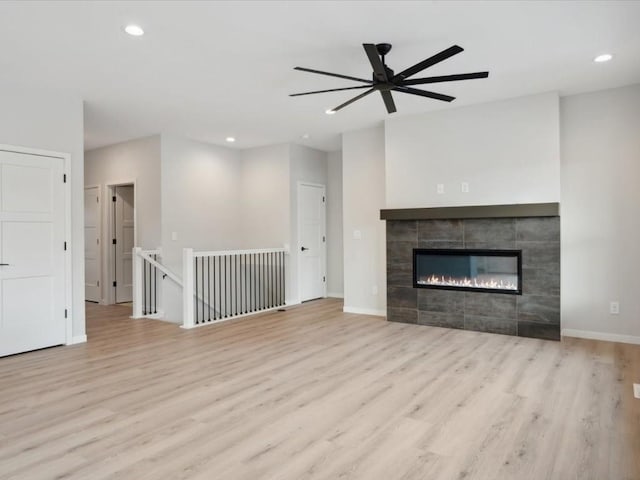 unfurnished living room with ceiling fan, a tile fireplace, and light hardwood / wood-style flooring