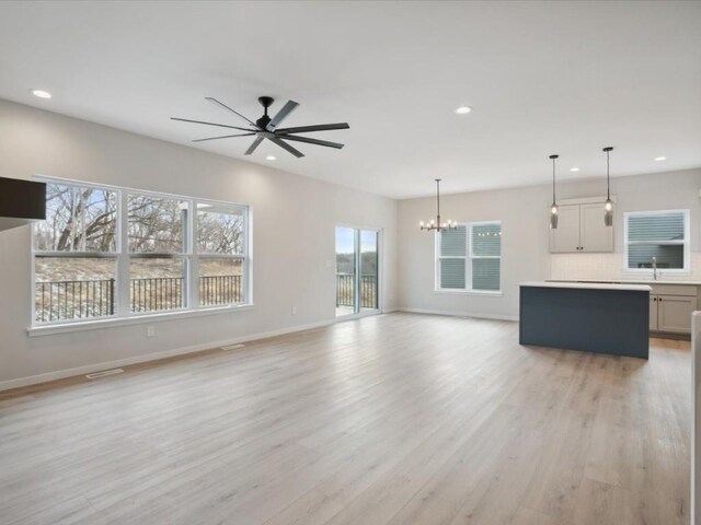 unfurnished living room featuring ceiling fan with notable chandelier, a healthy amount of sunlight, light wood-type flooring, and sink