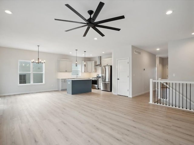 unfurnished living room featuring ceiling fan with notable chandelier and light hardwood / wood-style flooring