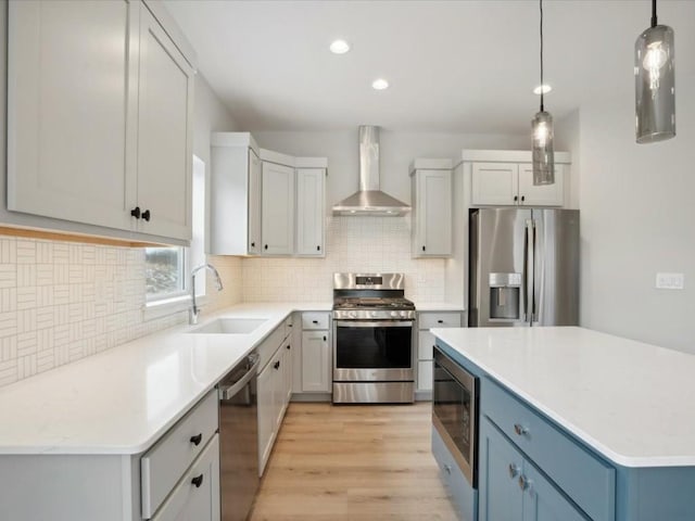 kitchen featuring wall chimney exhaust hood, stainless steel appliances, sink, decorative light fixtures, and white cabinets