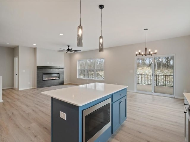 kitchen with a fireplace, stainless steel microwave, pendant lighting, and blue cabinets