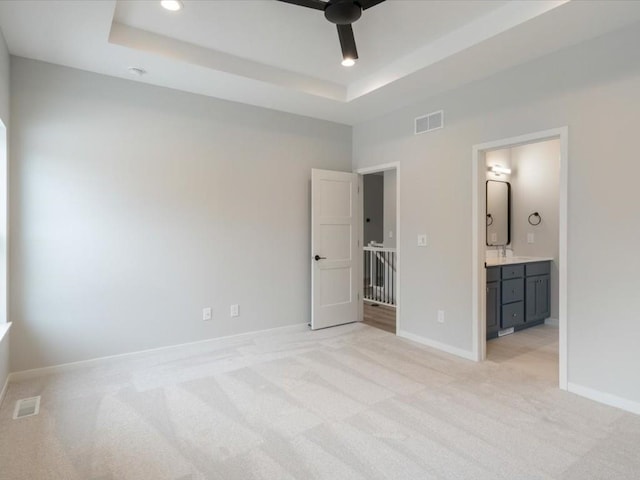 unfurnished bedroom featuring connected bathroom, light colored carpet, a raised ceiling, and ceiling fan