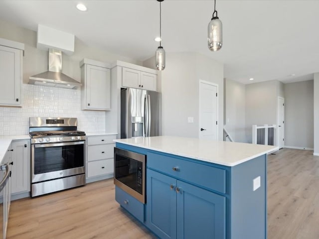 1423 Legend Dr, Tiffin, IA 52340 - kitchen featuring appliances with stainless steel finishes, wall chimney range hood, blue cabinetry, decorative backsplash, and light wood finished floors