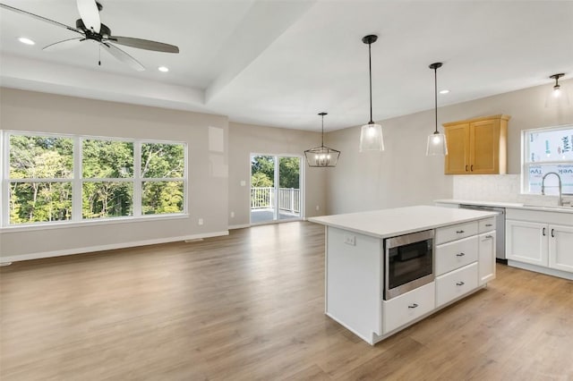 kitchen with white cabinetry, built in microwave, a center island, decorative light fixtures, and ceiling fan with notable chandelier