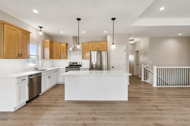 kitchen with wall chimney range hood, a kitchen island, appliances with stainless steel finishes, decorative light fixtures, and light hardwood / wood-style floors