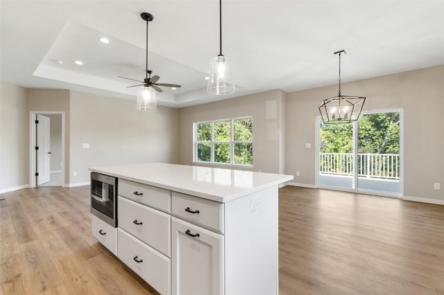 kitchen with built in microwave, a tray ceiling, decorative light fixtures, a kitchen island, and white cabinetry