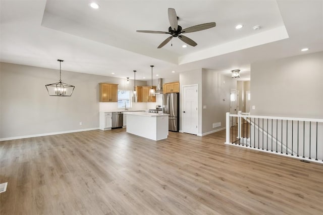 unfurnished living room featuring ceiling fan with notable chandelier, a tray ceiling, and light hardwood / wood-style floors