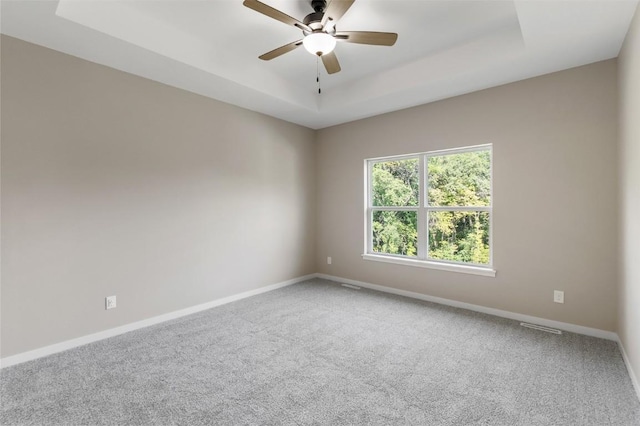 carpeted spare room featuring a raised ceiling and ceiling fan