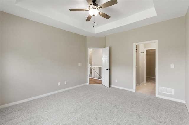 unfurnished bedroom with ceiling fan, a closet, a spacious closet, and a tray ceiling