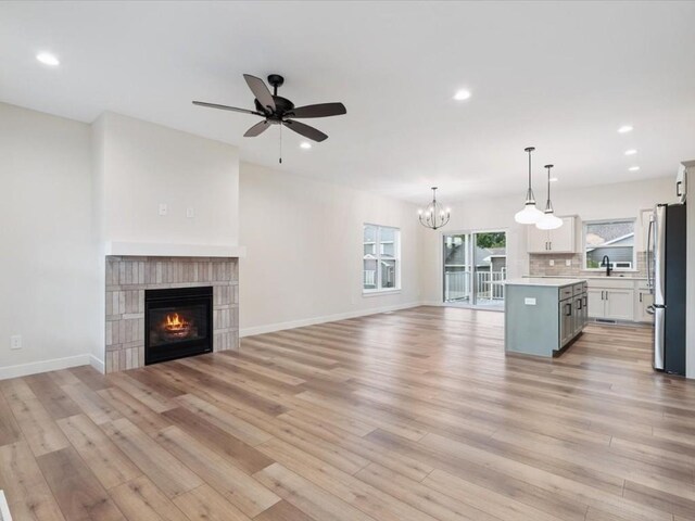 314 Sierra Trce, Coralville, IA 52241 - unfurnished living room with a tile fireplace, a chandelier, a ceiling fan, light wood-type flooring, and recessed lighting