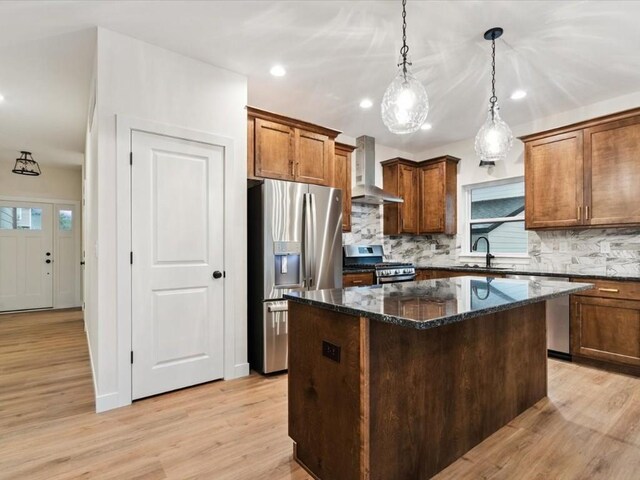 318 Sierra Trce, Coralville, IA 52241 - kitchen featuring appliances with stainless steel finishes, wall chimney exhaust hood, a kitchen island, decorative backsplash, and light wood-style flooring