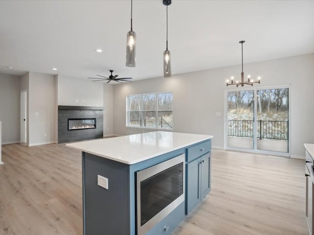 kitchen with a tile fireplace, blue cabinetry, decorative light fixtures, a center island, and stainless steel microwave