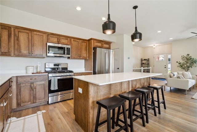 kitchen featuring light wood-type flooring, stainless steel appliances, a kitchen island, hanging light fixtures, and a breakfast bar area