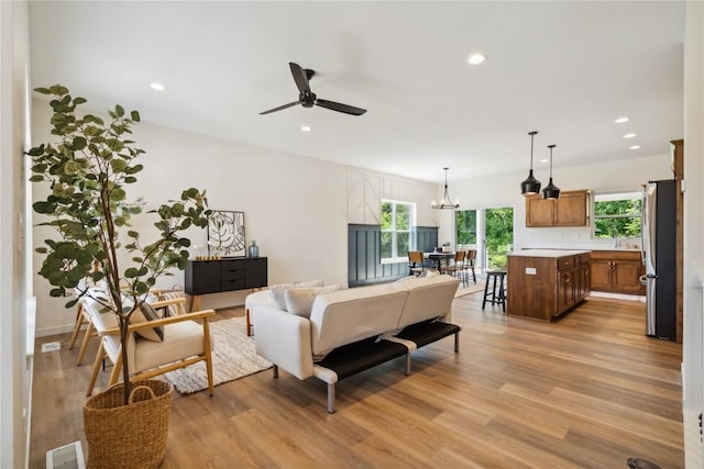 living room with ceiling fan with notable chandelier, light wood-type flooring, and sink