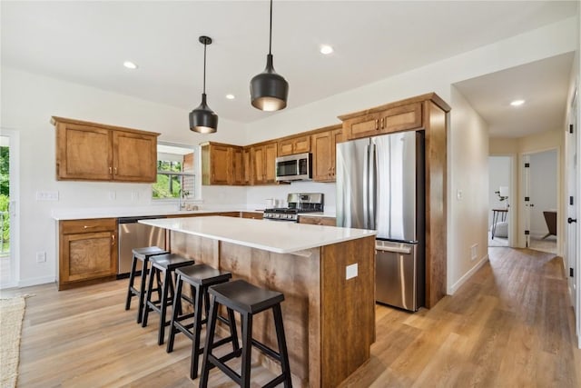 kitchen with sink, stainless steel appliances, pendant lighting, a kitchen island, and light wood-type flooring