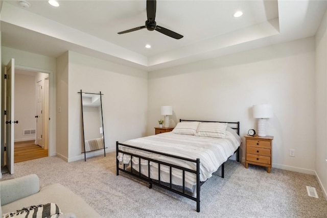 bedroom featuring light colored carpet, a raised ceiling, and ceiling fan