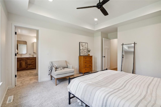 carpeted bedroom featuring a tray ceiling, ensuite bath, and ceiling fan