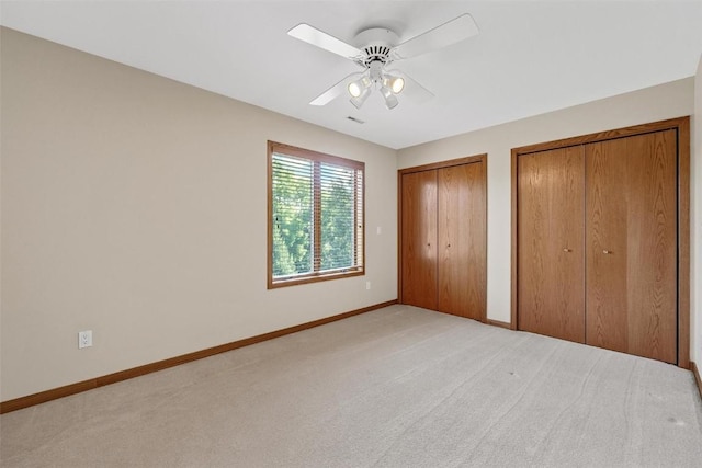 unfurnished bedroom featuring ceiling fan, light colored carpet, and two closets