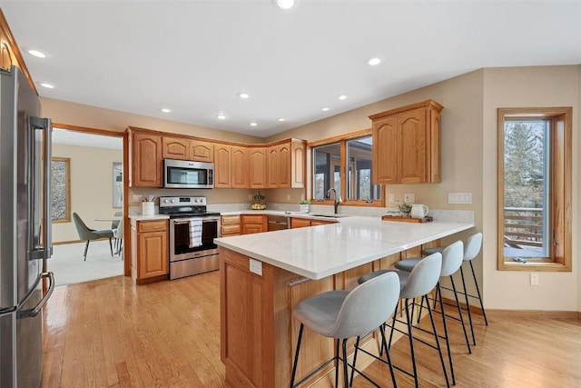 kitchen featuring sink, stainless steel appliances, kitchen peninsula, a breakfast bar area, and light wood-type flooring