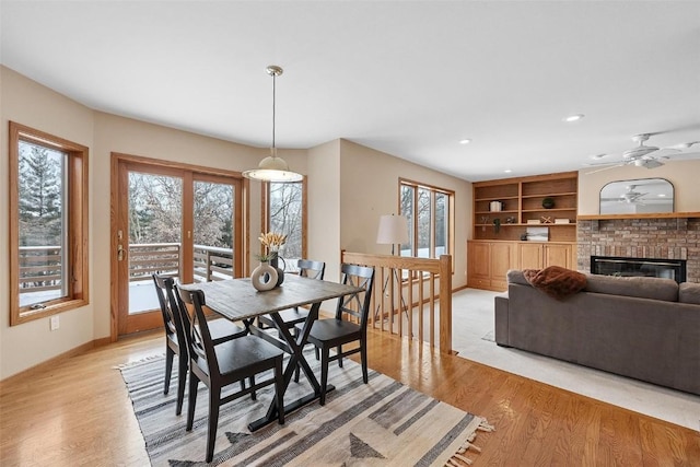 dining space featuring a brick fireplace, light hardwood / wood-style floors, built in features, and ceiling fan