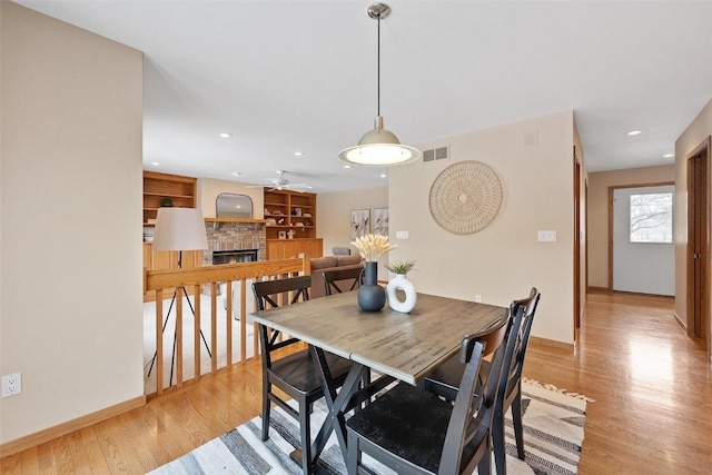 dining room with ceiling fan, built in shelves, a fireplace, and light hardwood / wood-style flooring