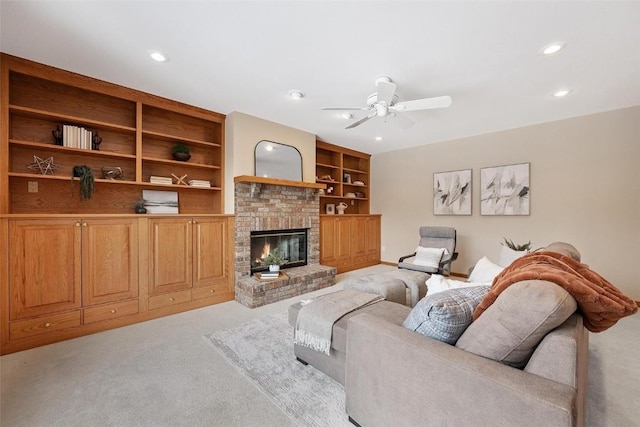 living room with a brick fireplace, light colored carpet, built in features, and ceiling fan