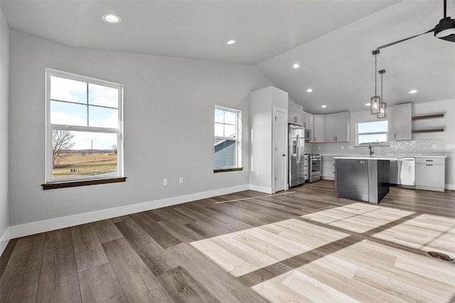 kitchen featuring pendant lighting, lofted ceiling, light wood-type flooring, appliances with stainless steel finishes, and a kitchen island