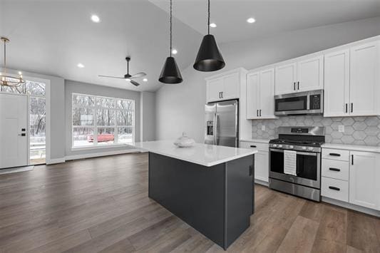 kitchen featuring tasteful backsplash, stainless steel appliances, decorative light fixtures, white cabinetry, and a kitchen island