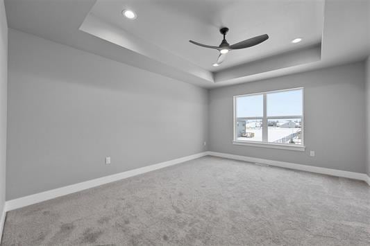 empty room featuring carpet flooring, ceiling fan, and a raised ceiling