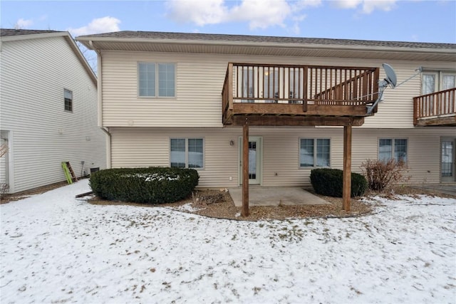 snow covered house with a patio area and a deck