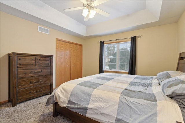 carpeted bedroom with a closet, a raised ceiling, and ceiling fan