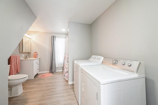 clothes washing area featuring sink, washer and clothes dryer, and light hardwood / wood-style floors