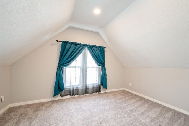 additional living space with lofted ceiling, carpet floors, and a textured ceiling