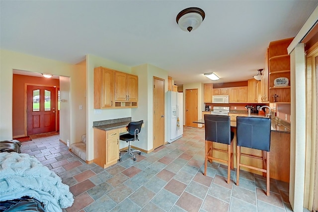 kitchen featuring built in desk, a kitchen bar, light brown cabinets, and white appliances