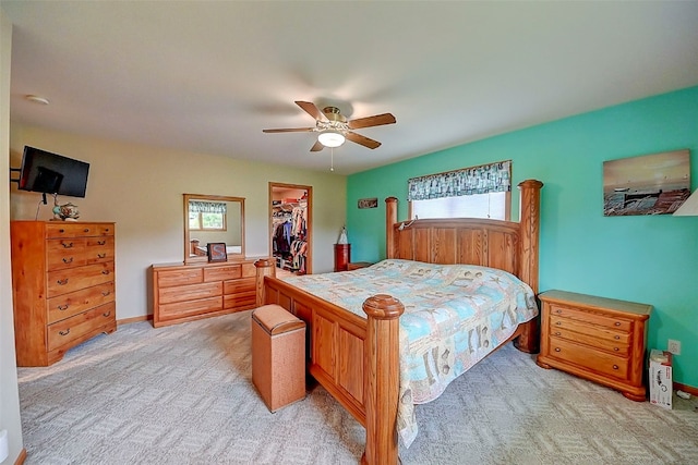 bedroom with a walk in closet, light colored carpet, ceiling fan, and a closet