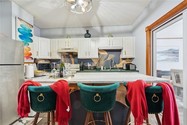 kitchen with a kitchen bar, stainless steel refrigerator, sink, and white cabinets