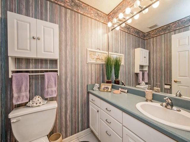 bathroom with visible vents, toilet, vanity, tile patterned flooring, and wallpapered walls