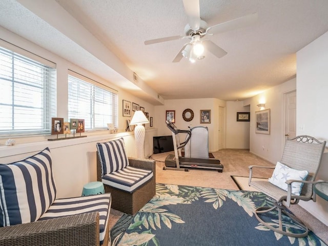 living area featuring a ceiling fan, light colored carpet, and a textured ceiling