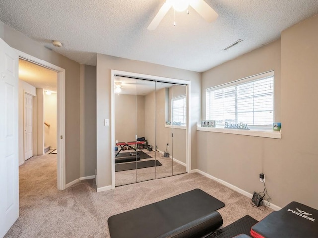 workout area featuring a textured ceiling, carpet flooring, visible vents, and baseboards