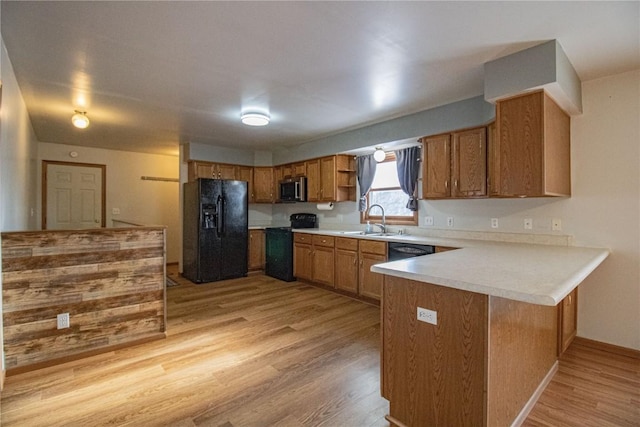 kitchen with black appliances, light wood-type flooring, kitchen peninsula, and sink